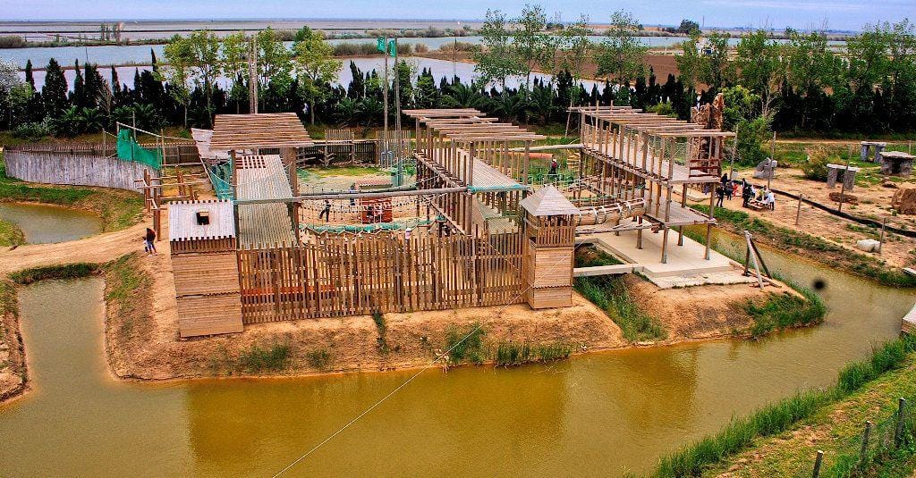 Imagen aérea de los puentes tibetanos del parque de aventuras en Deltebre, mostrando las plataformas, cuerdas y circuitos de altura en plena naturaleza del Delta del Ebro.