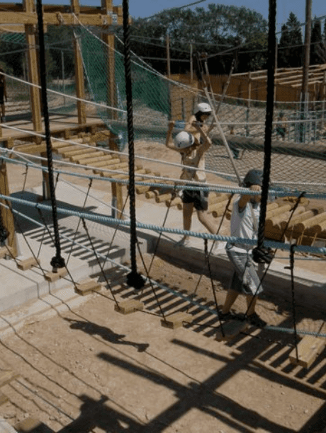 Niños cruzando cuerdas y maderas en el circuito de puentes tibetanos del parque de aventuras en Deltebre, disfrutando de actividades de equilibrio y adrenalina.